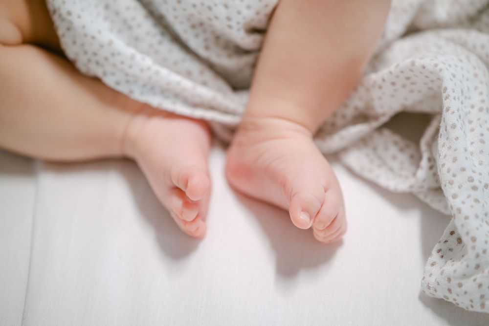 Close up view of tiny bare baby feet against white polka dot fabric background.