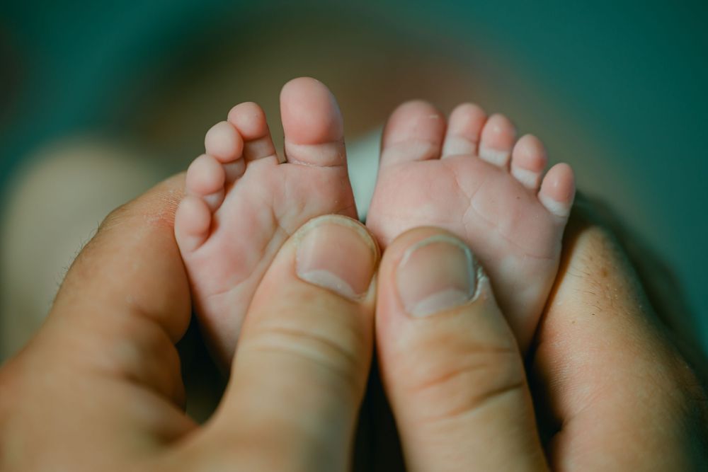 Close-up of tiny baby toes with wrinkled skin texture against a dark teal background.
