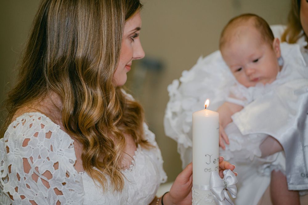 A tender moment between parent and child during a christening ceremony with white lace and candlelight.