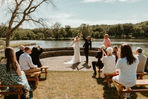 An outdoor wedding ceremony by a lake with guests seated on wooden benches.