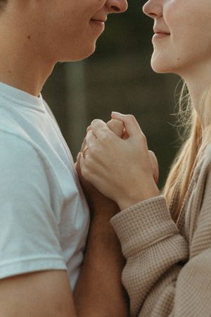 Two people share an intimate close-up moment holding hands with soft natural lighting.