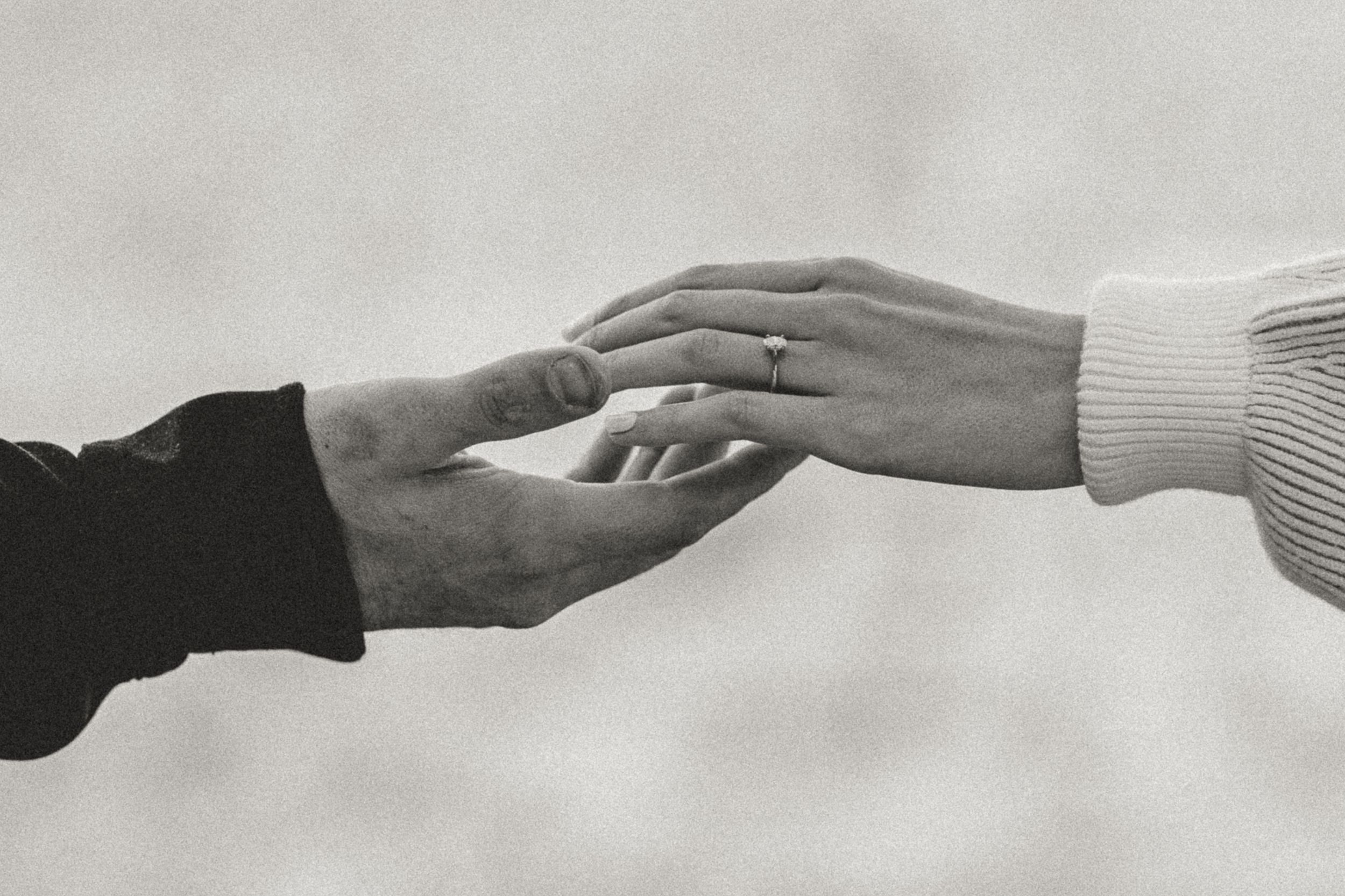 Two hands reaching toward each other in a tender black and white photograph.