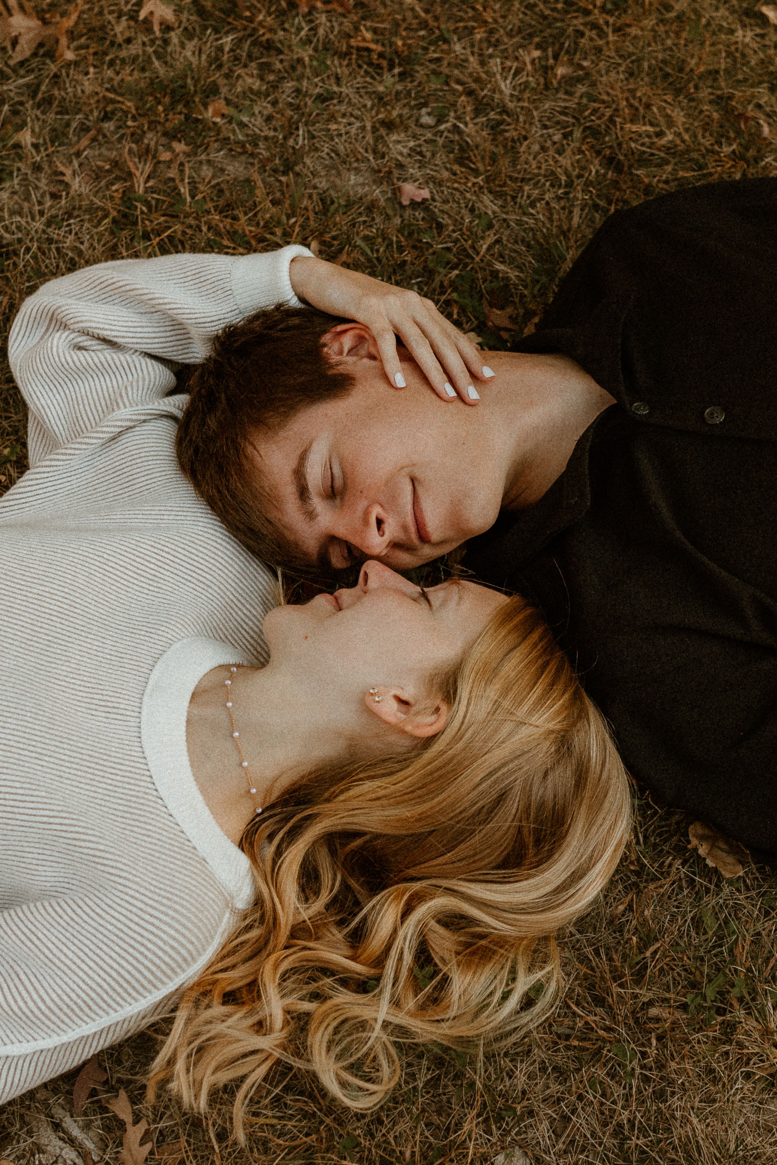 An intimate portrait of a couple lying on grass with their heads together.