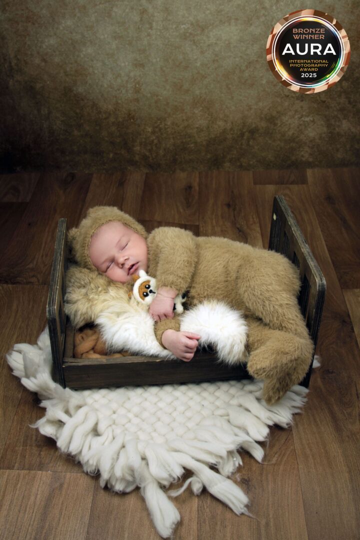 Sleeping baby in bear costume cuddles with white fur in wooden crate.