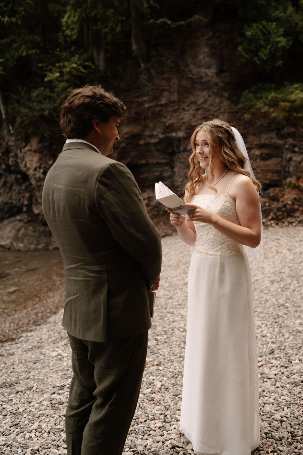 A couple sharing an intimate wedding ceremony moment while reading notes on a rocky beach.