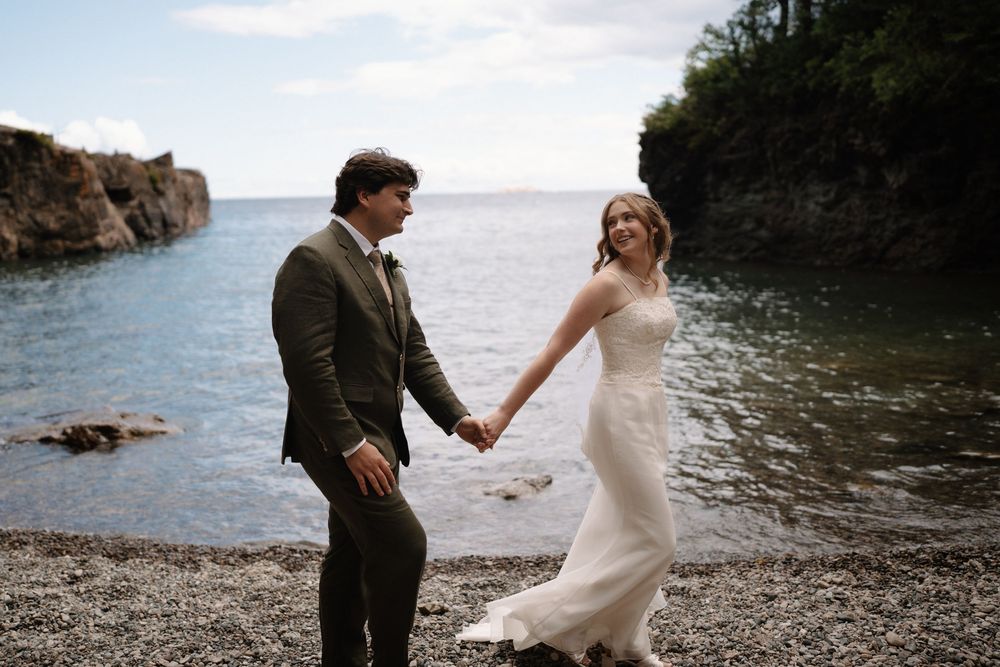 Newlywed couple poses for romantic photos on rocky beach with dramatic ocean backdrop and cliffs in Maine.