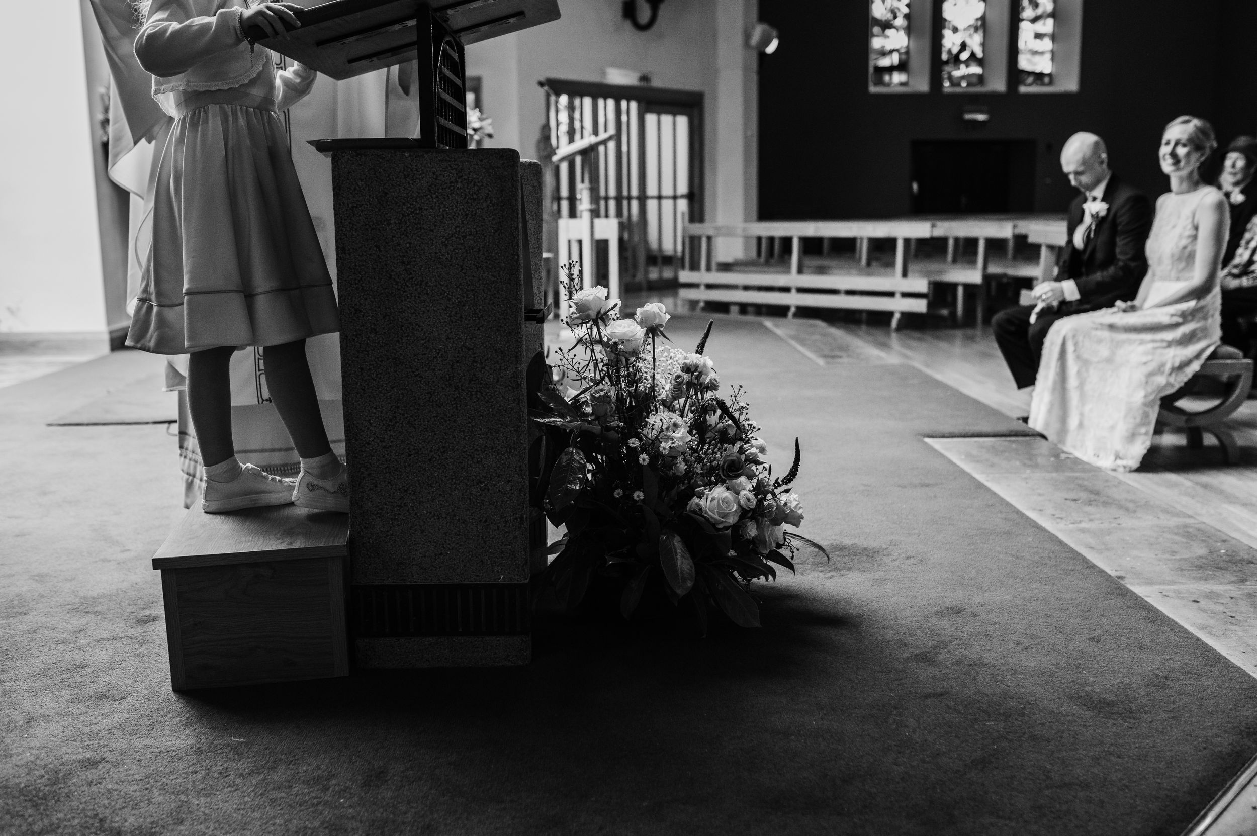 A black and white photo of a performance space with piano and floral arrangements.