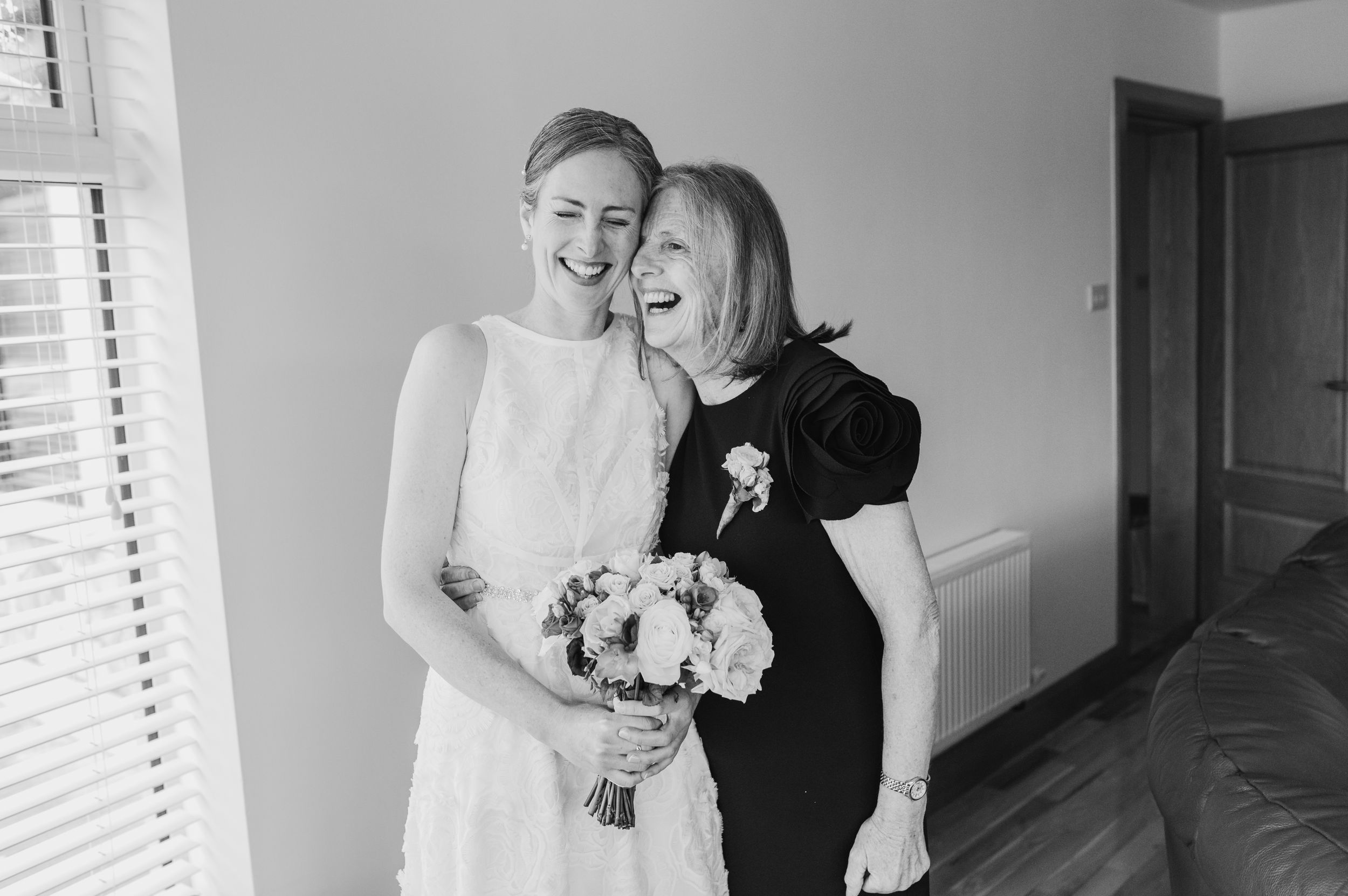 A black and white candid moment showing two people sharing joy while holding a bouquet.