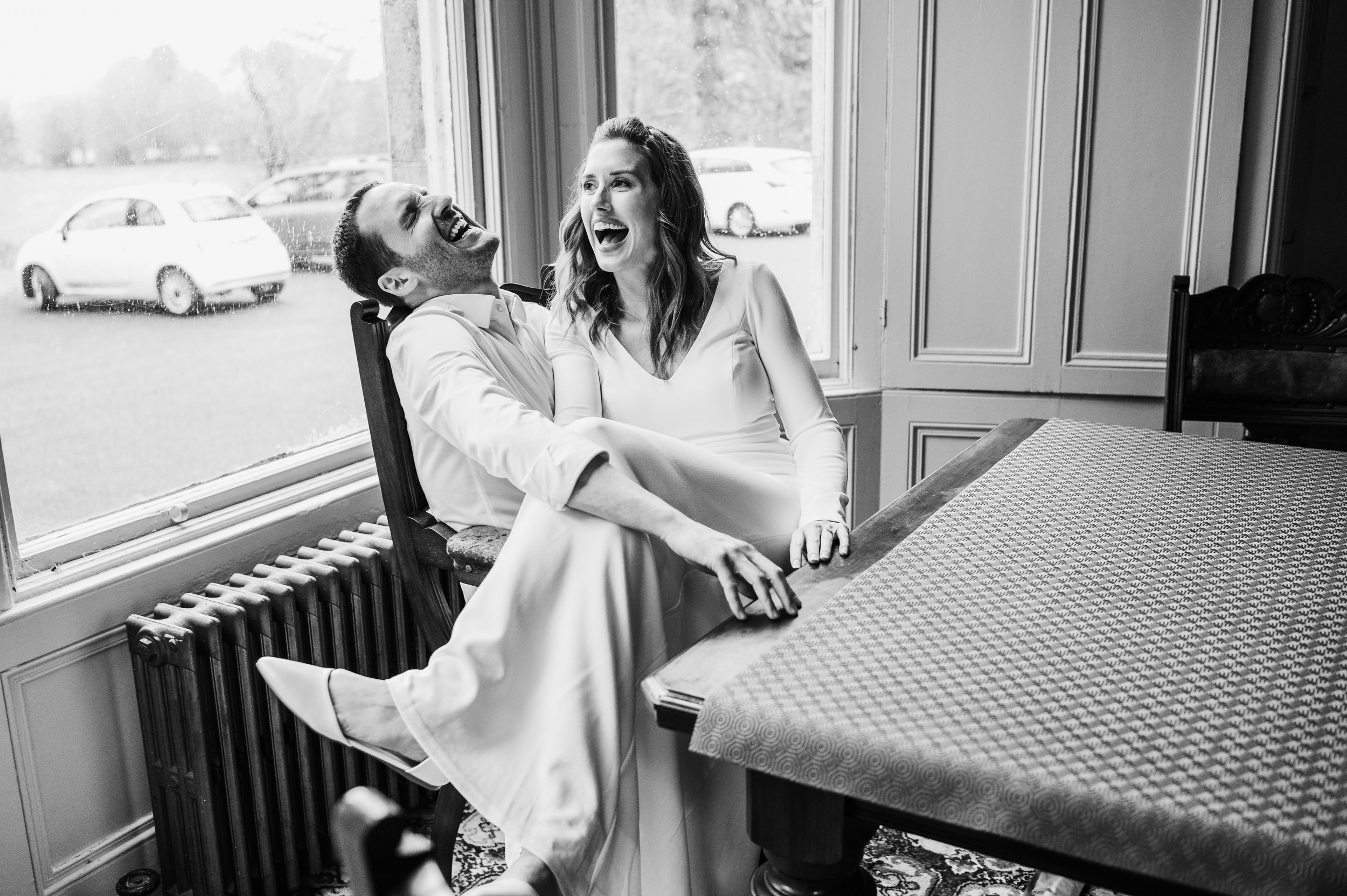 A bride in a white wedding dress laughs and poses with her bridesmaids on a restaurant patio.