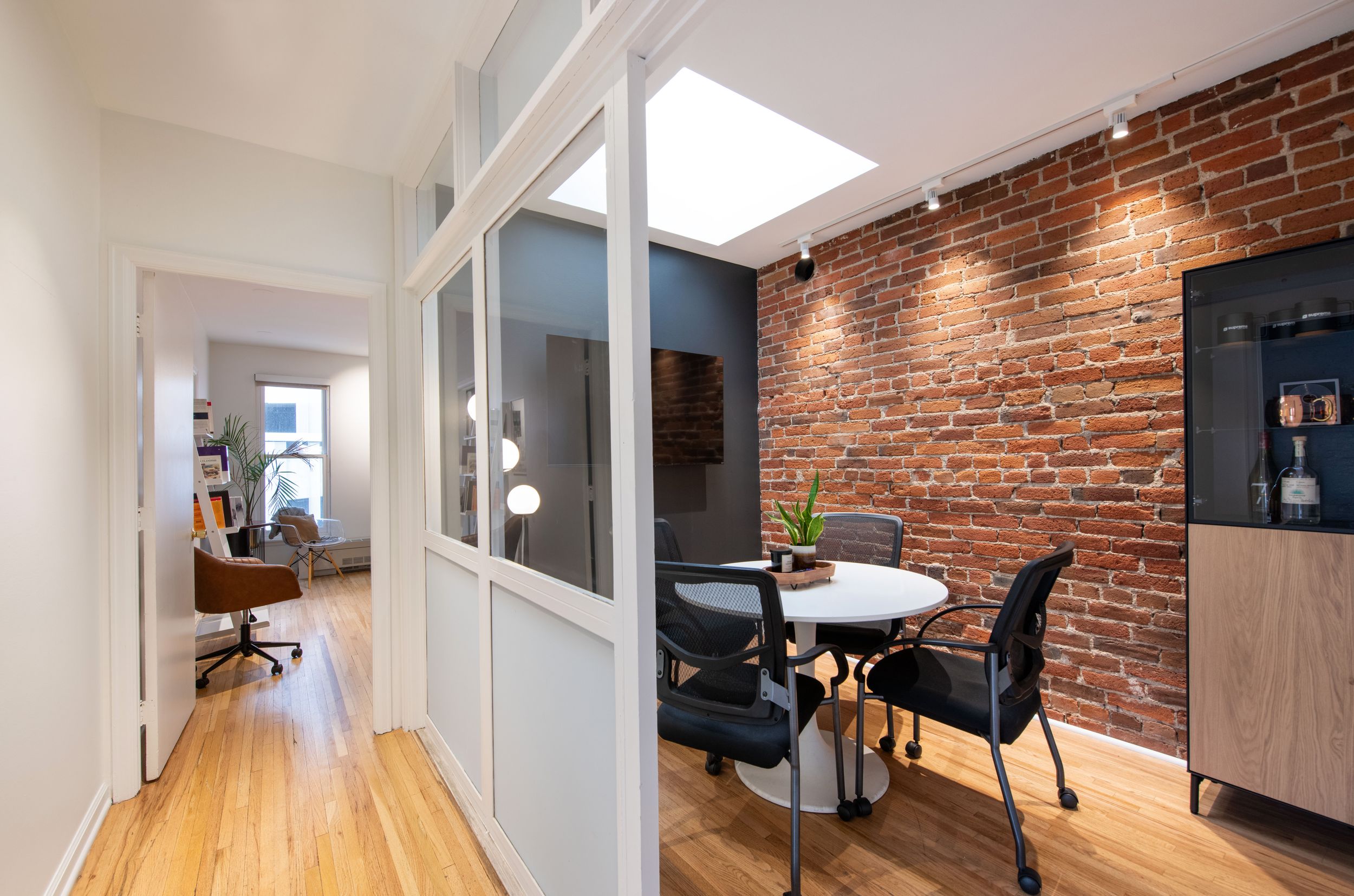 Modern office hallway with exposed brick wall, glass partition, and round dining table.