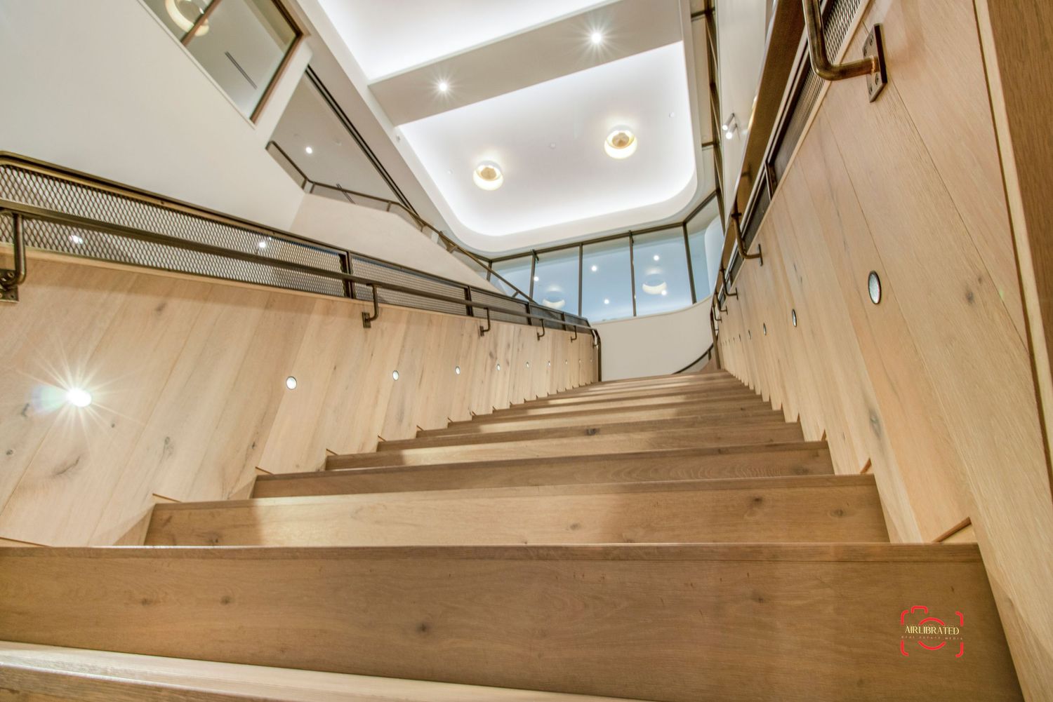 Looking up a modern wooden staircase with metal handrails and recessed lighting.