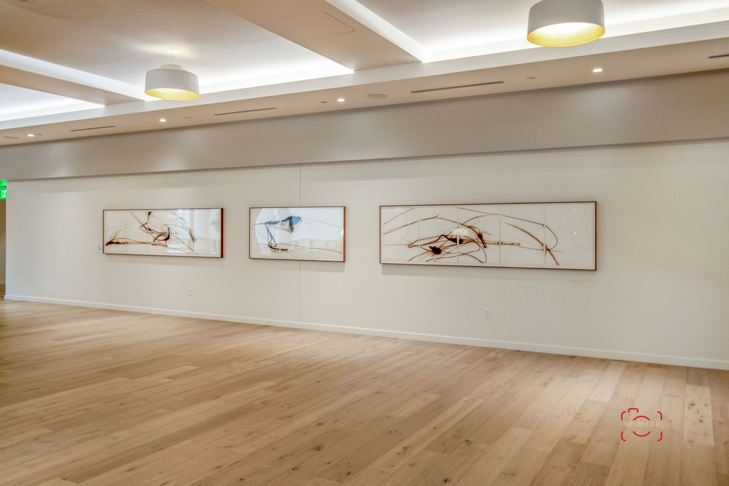 Minimalist gallery wall with three framed artworks in a modern space with wooden floors.