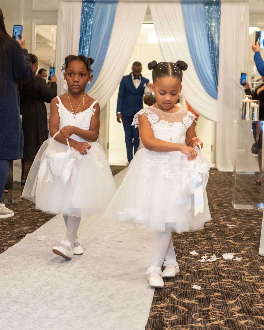 Two flower girls in white tulle dresses walking down aisle during wedding ceremony.