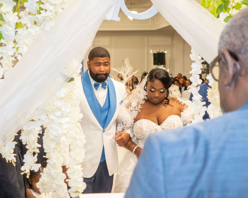 Wedding ceremony under white floral arch with couple and officiant at elegant outdoor venue.