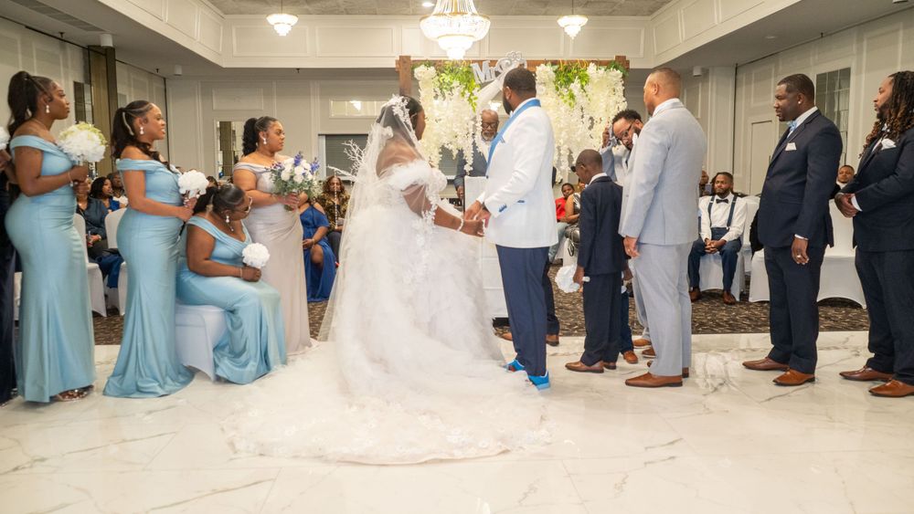 Wedding party in light blue bridesmaid dresses and formal attire gathered in elegant venue during ceremony.