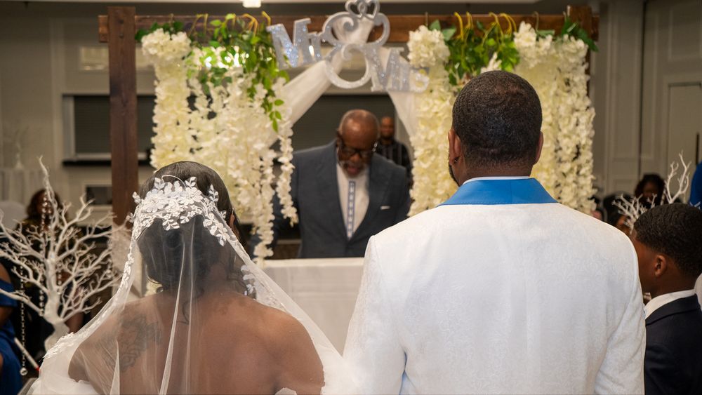 A wedding ceremony under an elegant white floral arch with decorative branches.