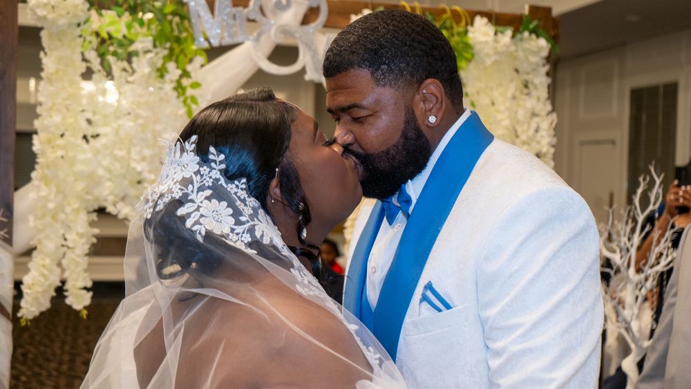 A tender moment between newlyweds under a floral arch at their wedding celebration.