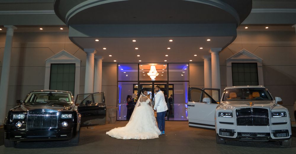 Luxury cars flank a wedding venue entrance with purple lighting and elegant decor.