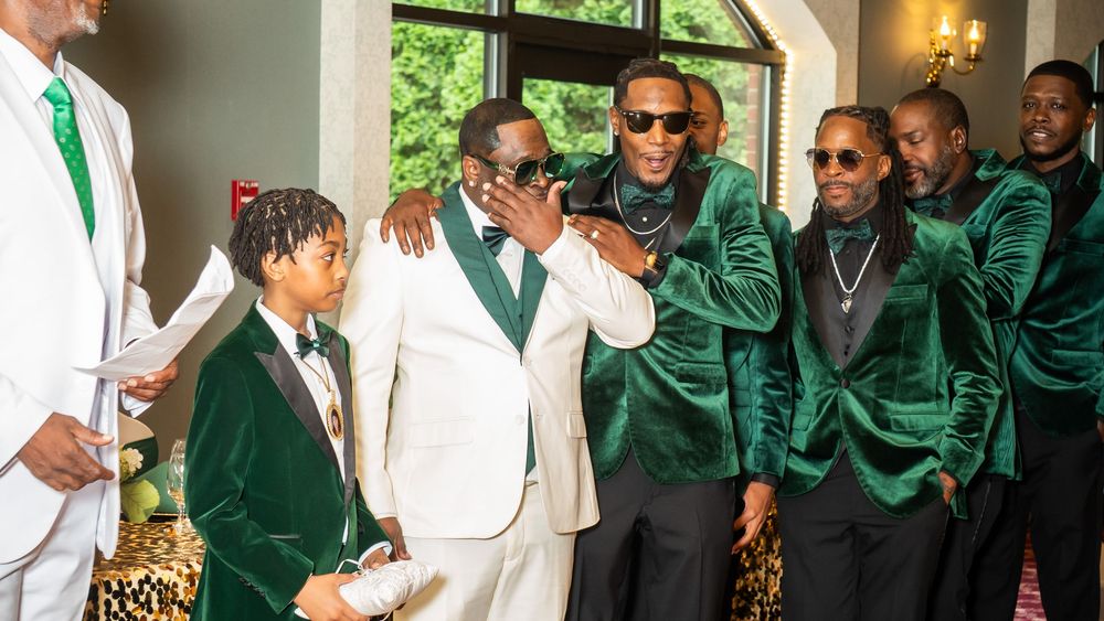 Group of men in elegant green velvet suits and white tuxedo posing together at a formal celebration event.