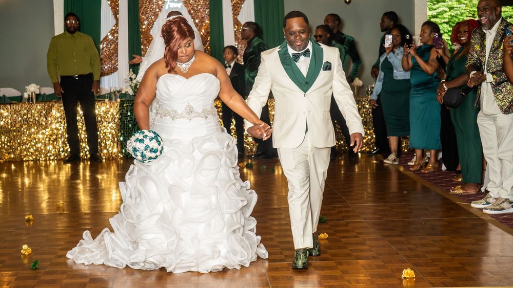 Newlyweds share first dance, bride holding green bouquet, groom in cream suit with emerald green lapels.