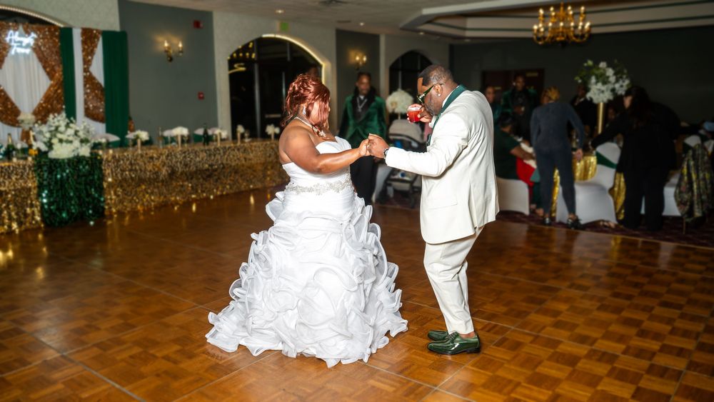 Bride and groom share their first dance in an elegant ballroom decorated with gold and green accents at their wedding reception.