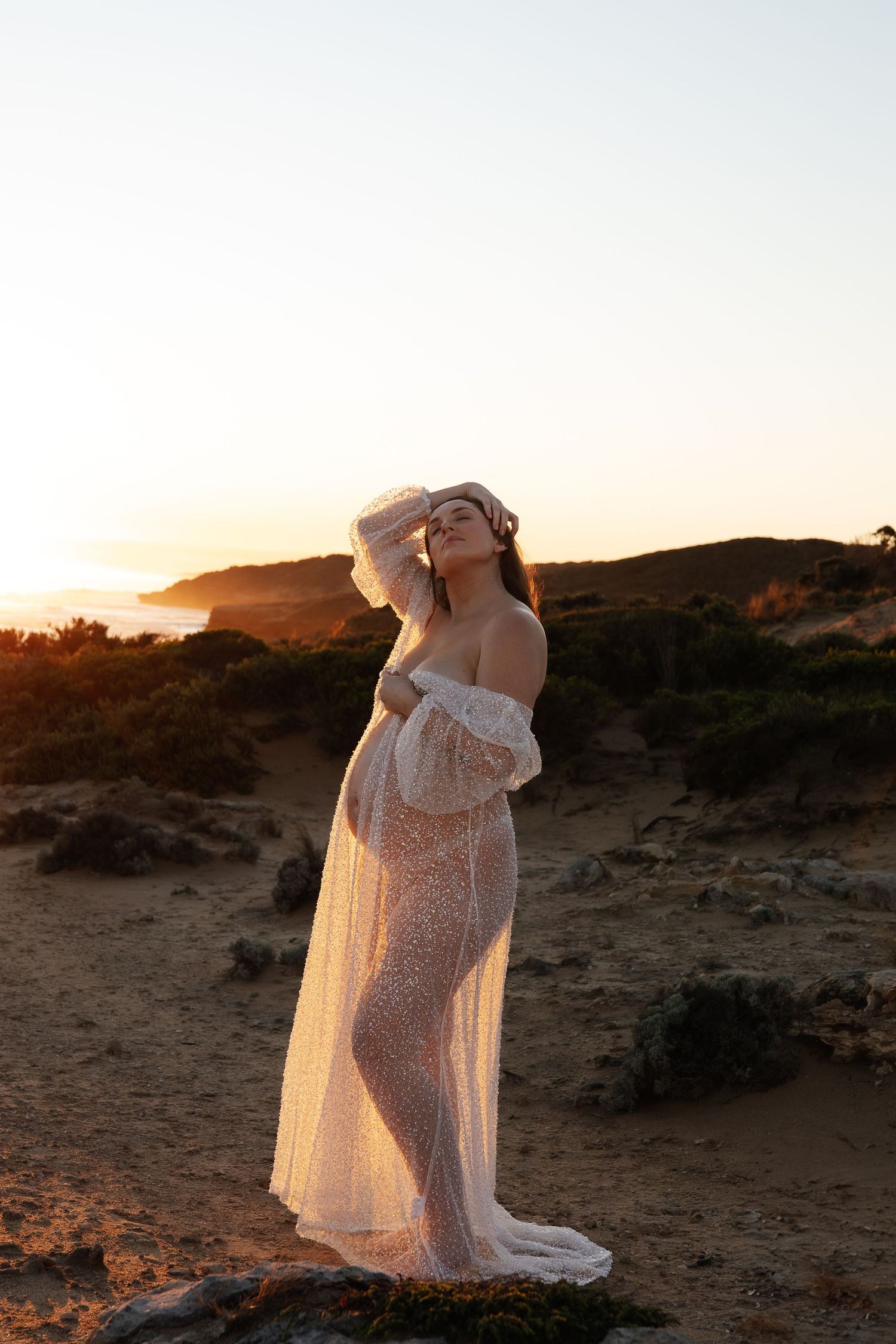 Maternity photo on rocky beach shore during golden hour.