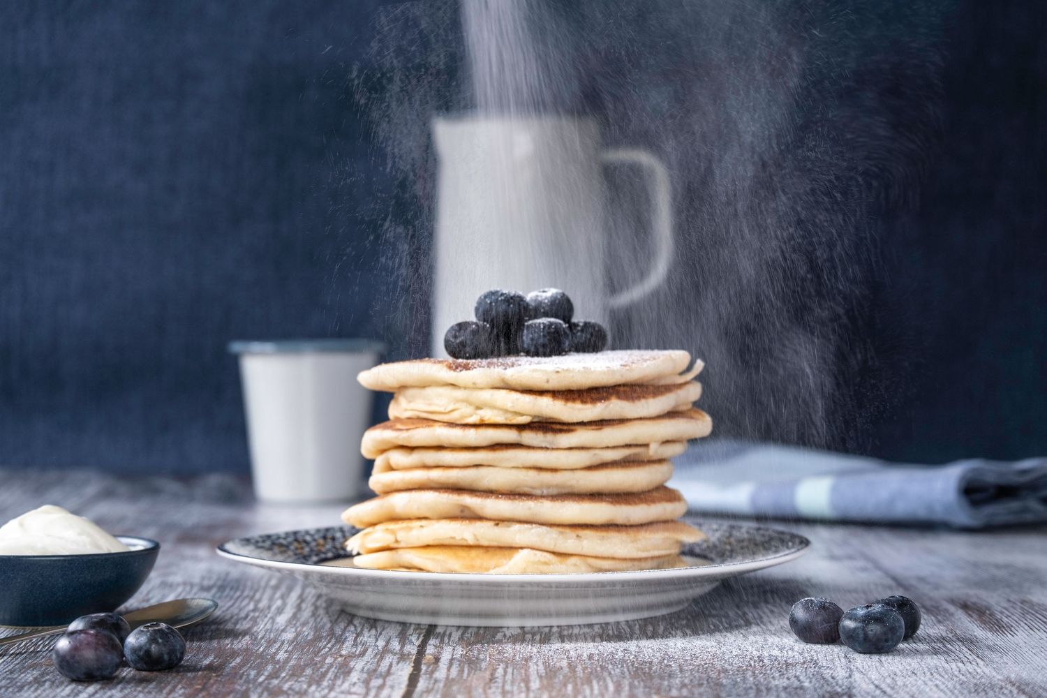 Icing sugar being dusted onto a stack of home made pancakes