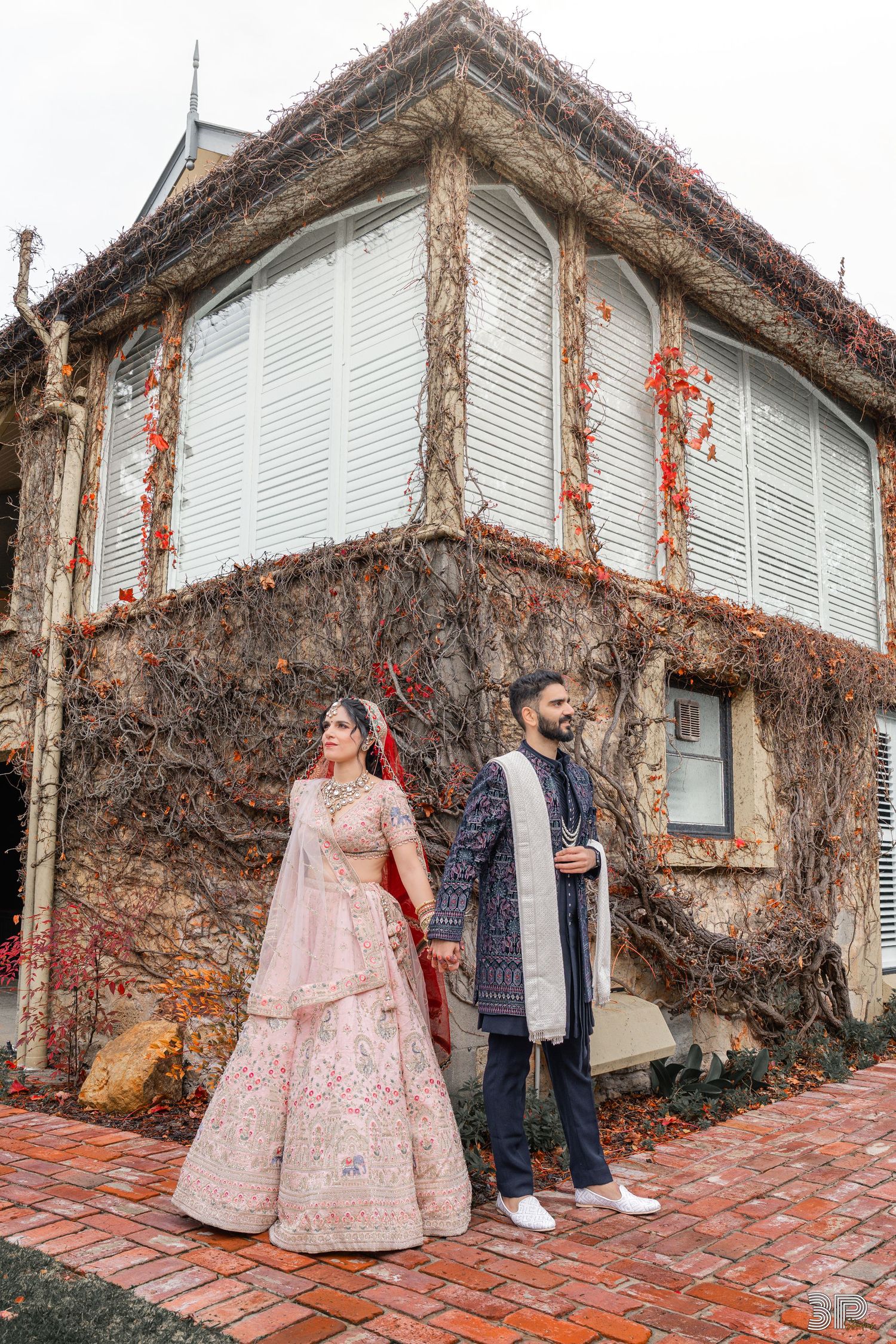 A couple in traditional South Asian wedding attire sits together on an elegant blue sofa with pink floral decorations.