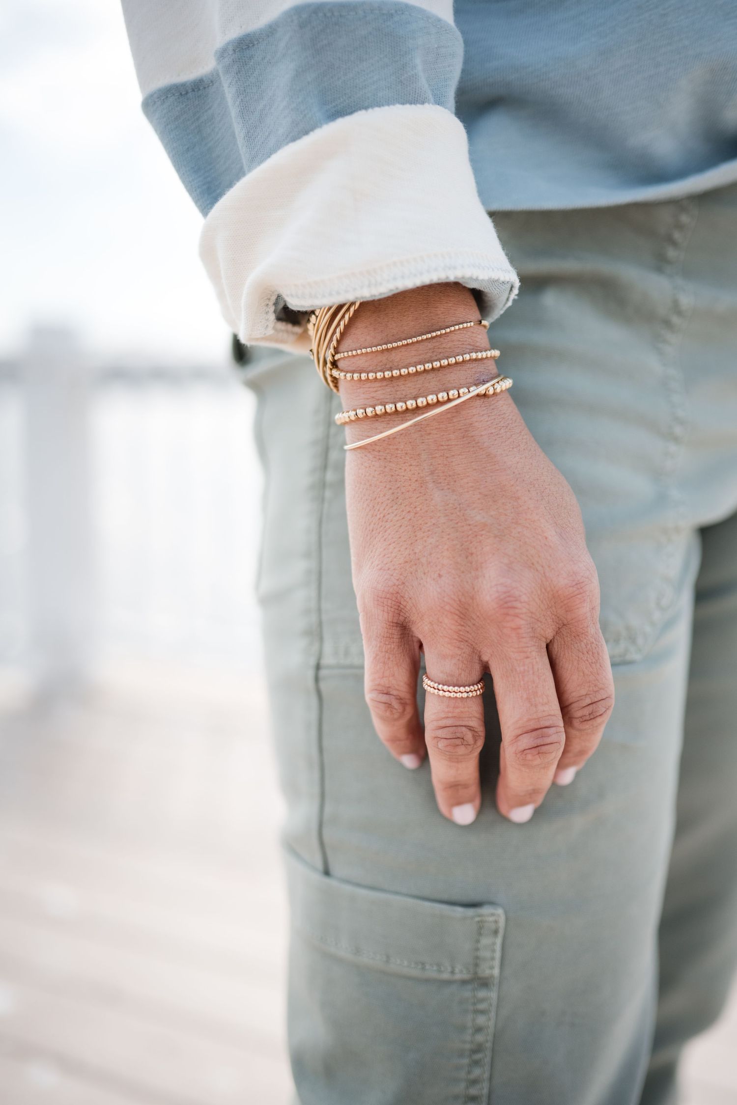 Close-up of delicate gold bracelets and rings styled with casual clothing.