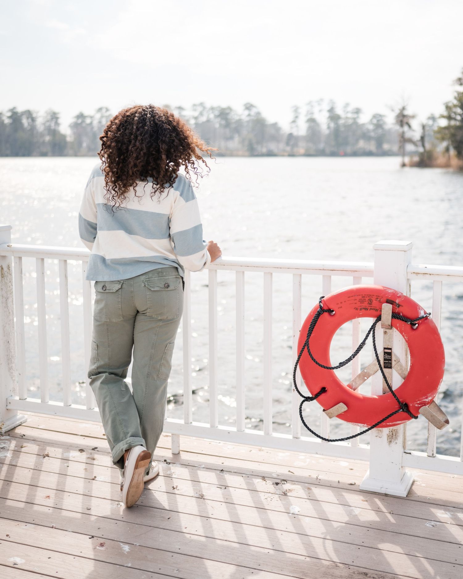 Back view of person looking out over water from white deck with red life preserver.