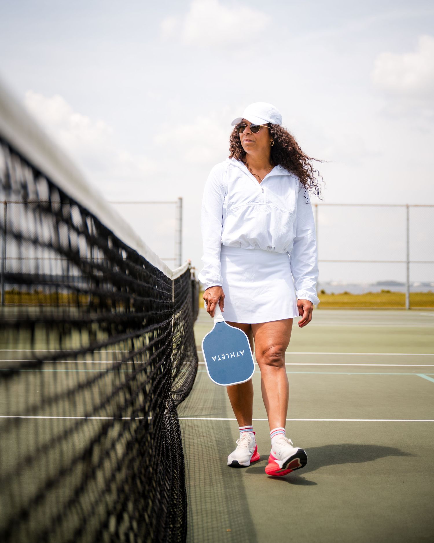 Tennis player wearing white outfit and blue shorts stands on court next to black net.