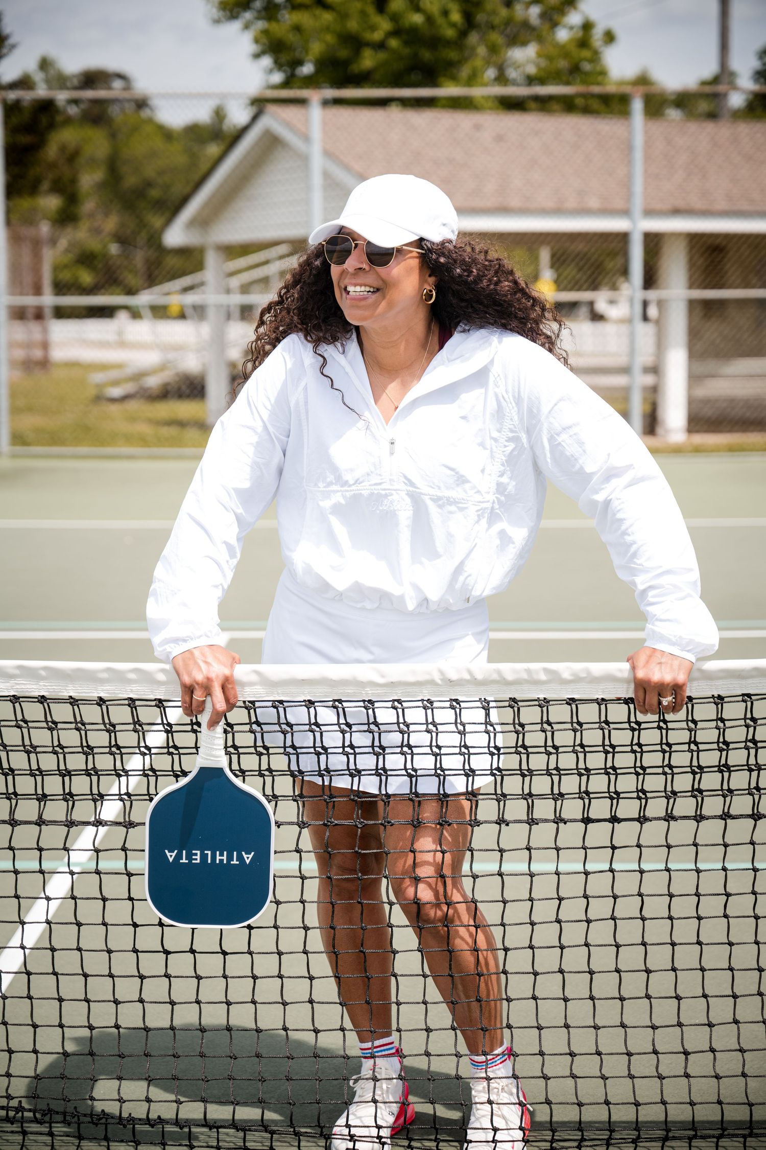 Lifestyle shot of tennis player with Athleta paddle at court net.