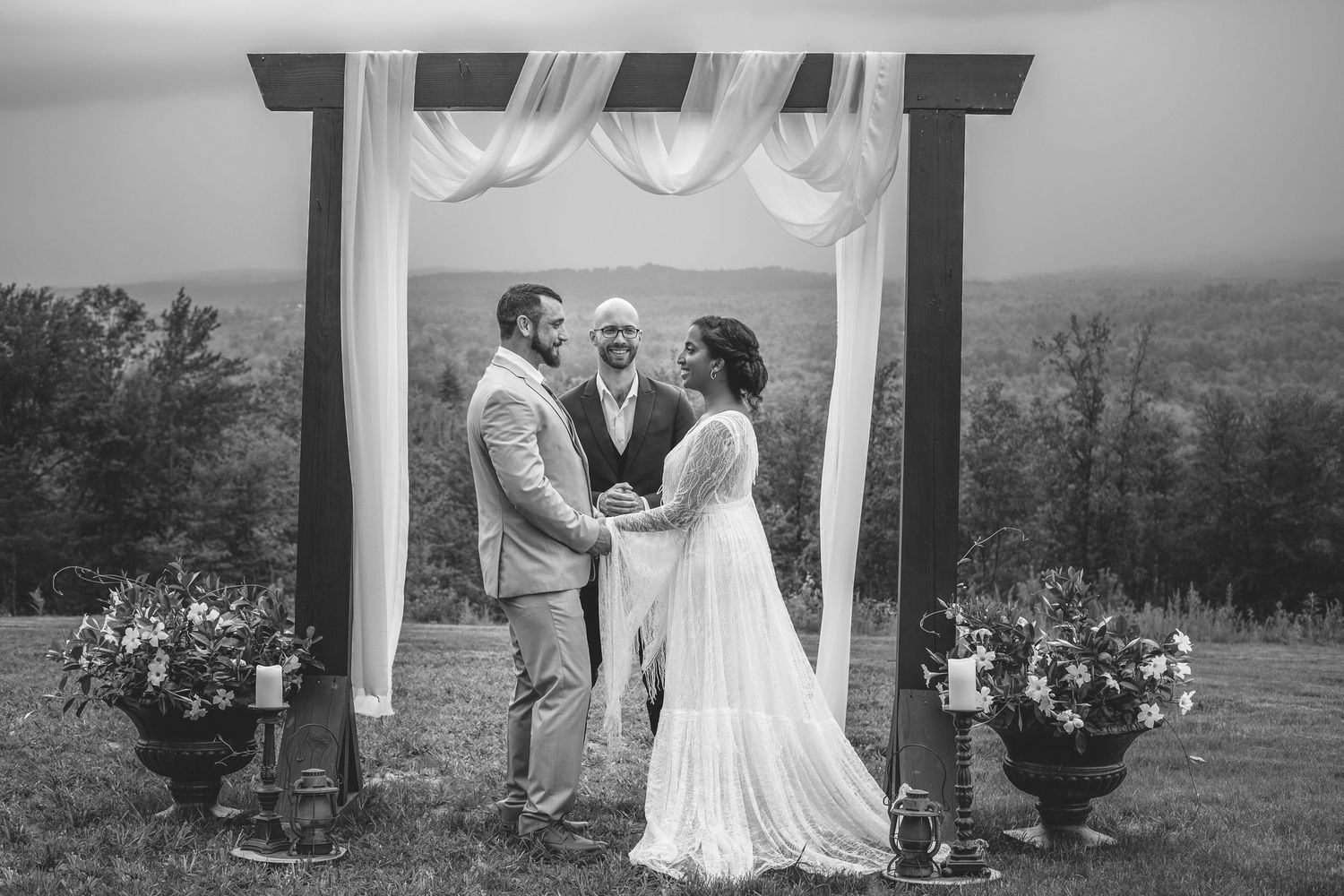 Black and white wedding ceremony under a draped arch with mountain views.