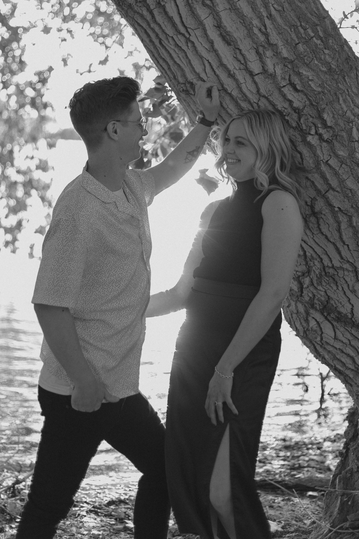 Couple sharing intimate moments beneath tree branches in black and white photography.