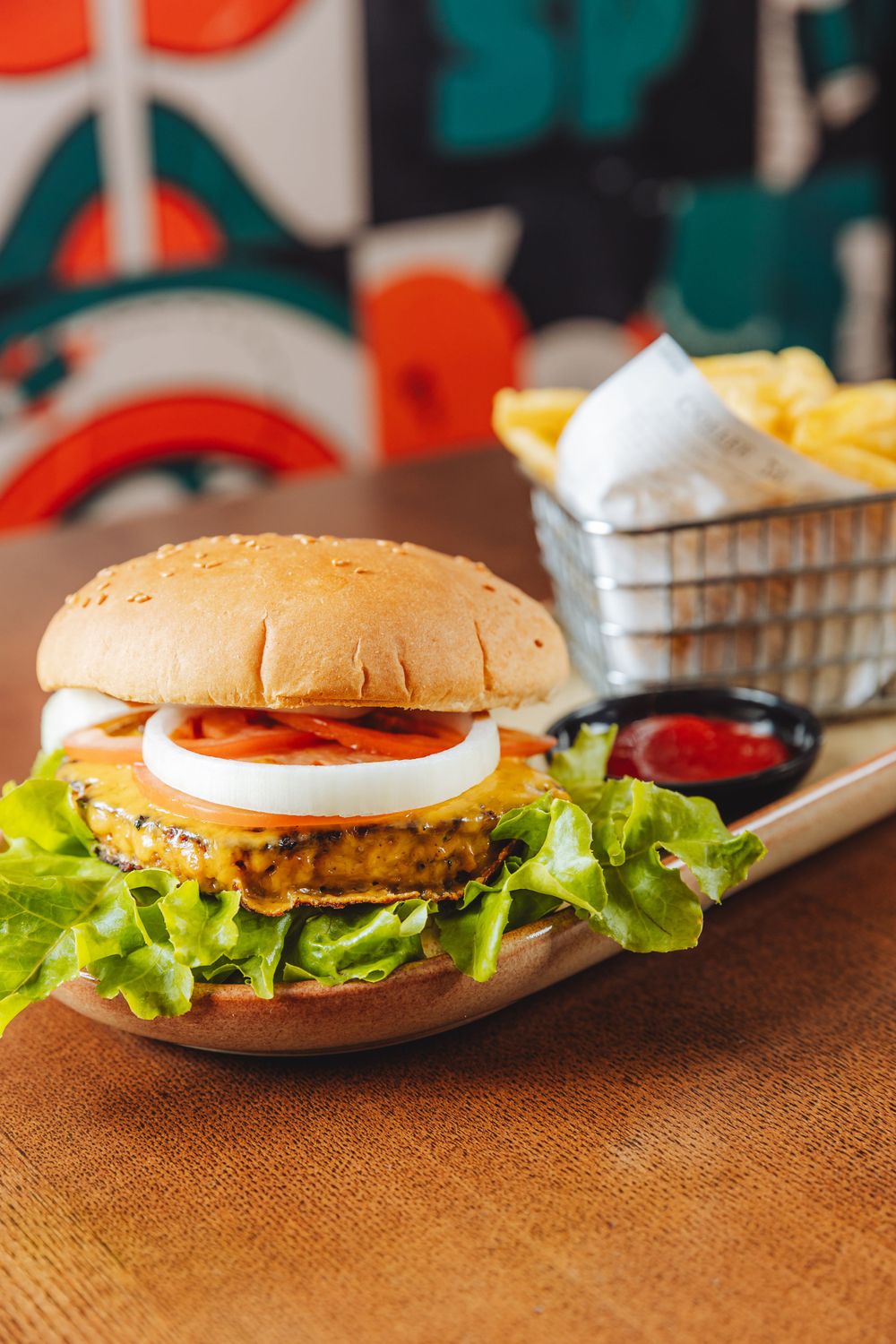 A veggie burger with fresh lettuce, tomato and onion served on a bun alongside french fries and dipping sauce.
