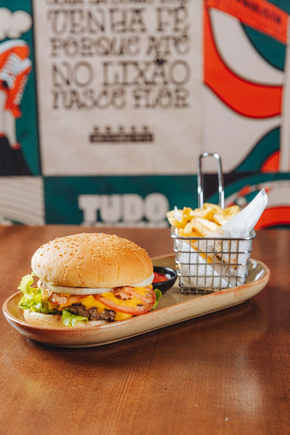 Juicy cheeseburger with lettuce and melted cheese served on wooden plate with side basket of french fries.