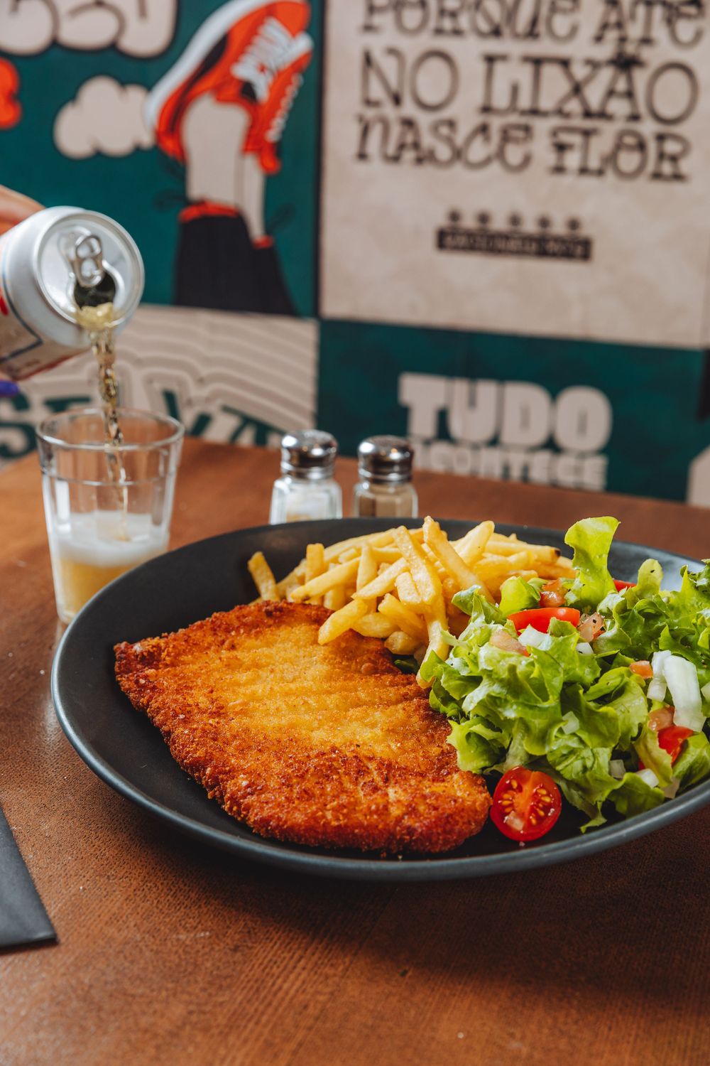 A crispy breaded schnitzel served with french fries and fresh garden salad on a black plate at a restaurant.