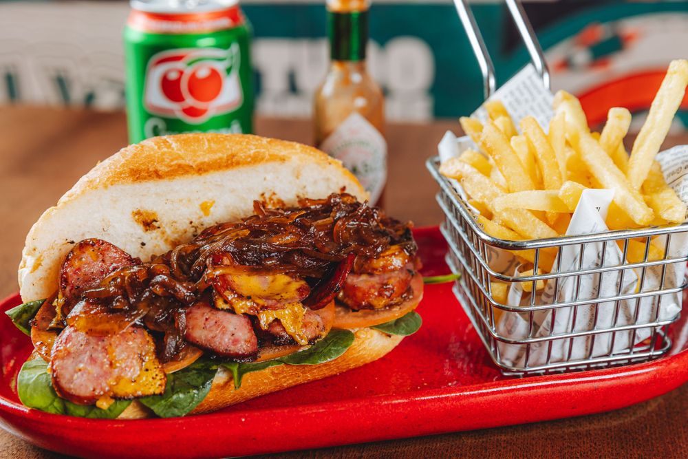 A juicy BBQ pull pork sandwich served on a red plate with a side basket of crispy french fries and a soda.
