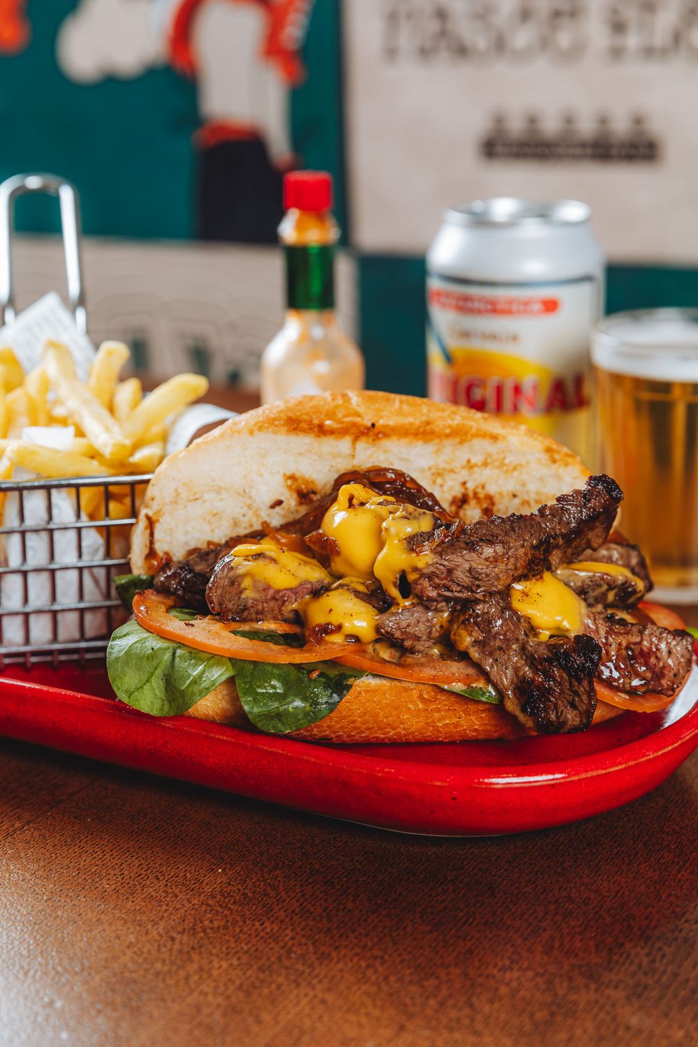 Juicy cheeseburger with melted cheese and french fries served on red plate with beer cans in background.