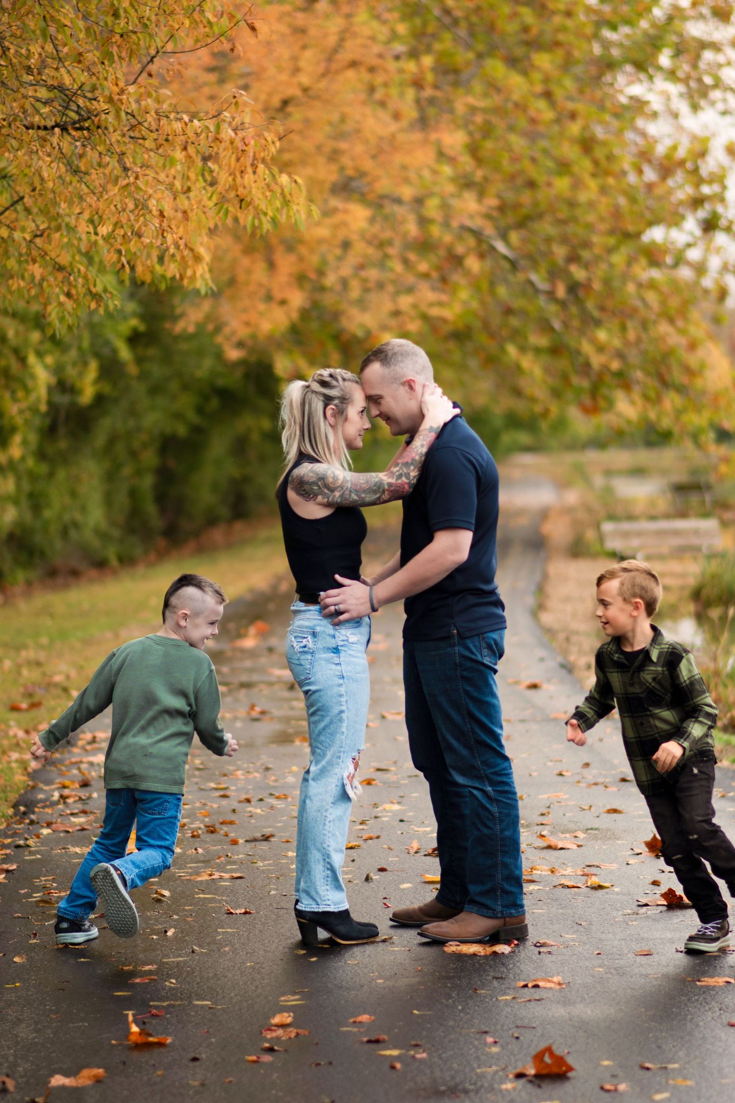 Parents sharing a romantic moment while two young boys run around them in autumn park.