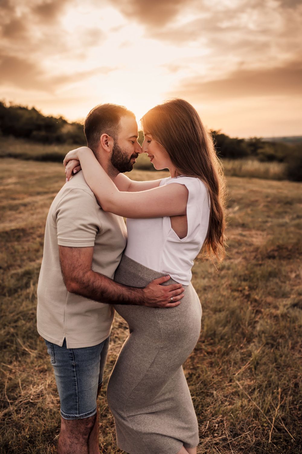 A romantic sunset embrace between a couple in a rural field with warm golden light illuminating the scene.
