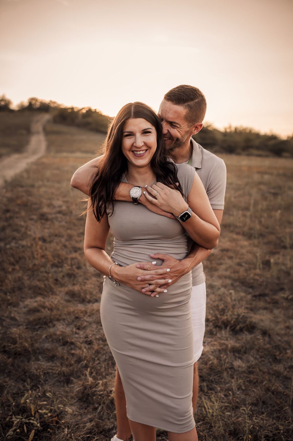 Couple embraces in romantic sunset photoshoot on a hill with golden light and warm earth tones.