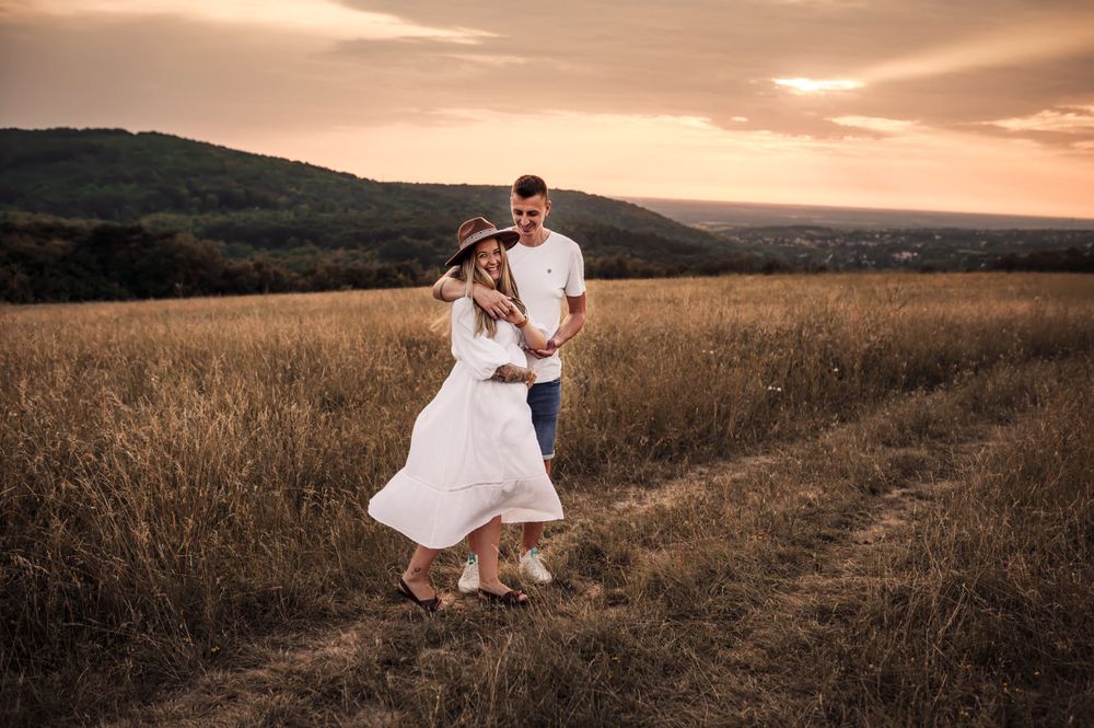 A couple dancing in a golden field at sunset with mountains in the background.
