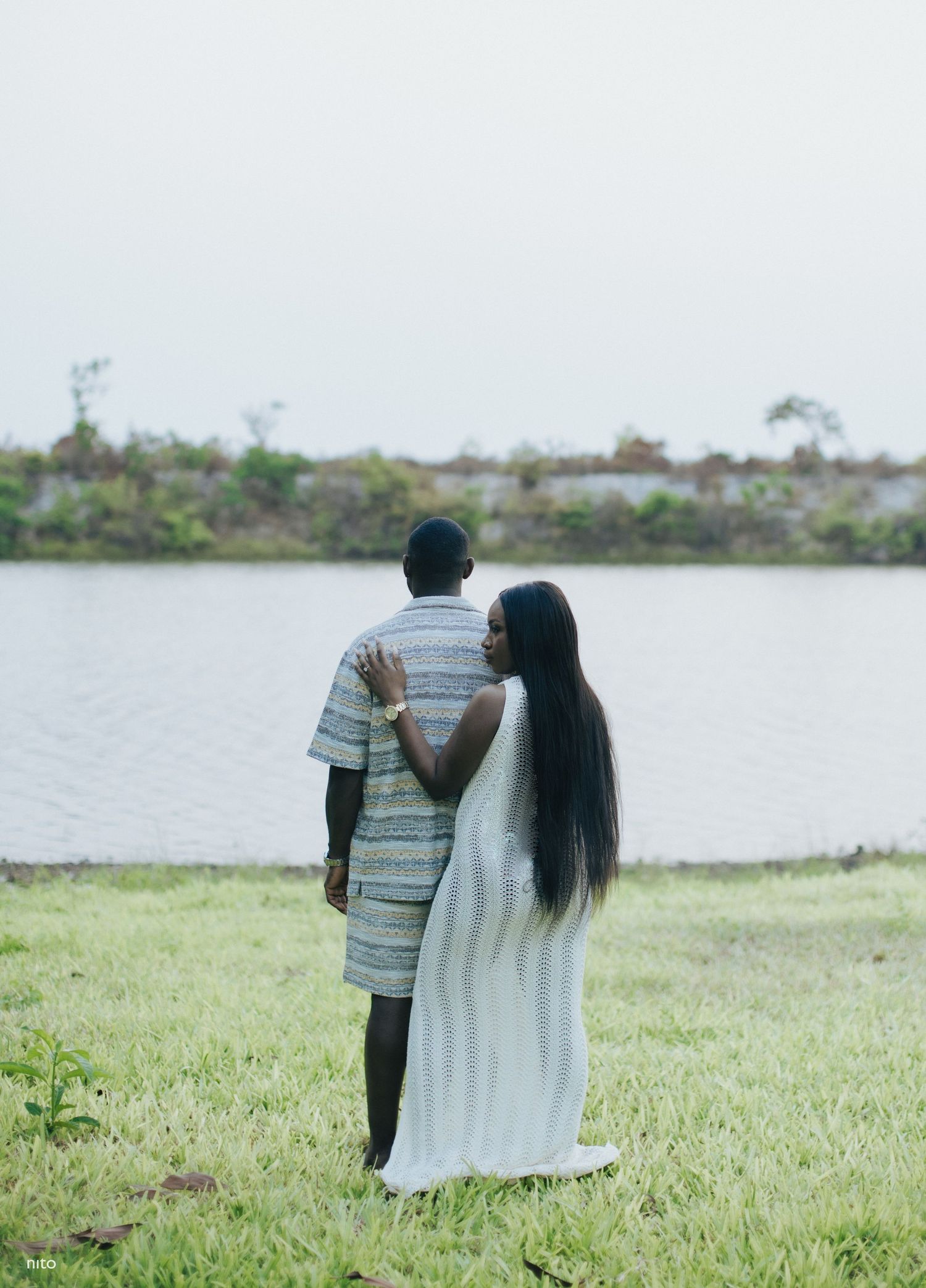 Couple stands together near a lake, sharing an intimate moment in nature.