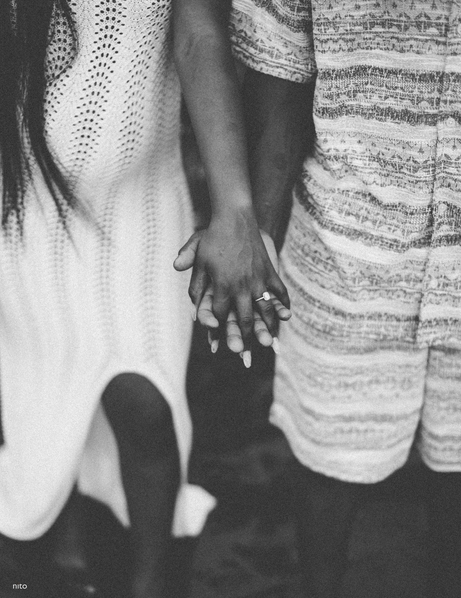 Black and white photo of two people holding hands while wearing formal attire.