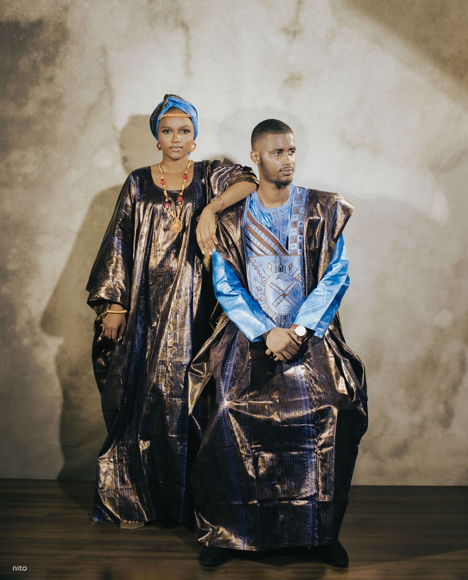 A couple poses in traditional African formal wear featuring rich metallic fabrics and blue accents.