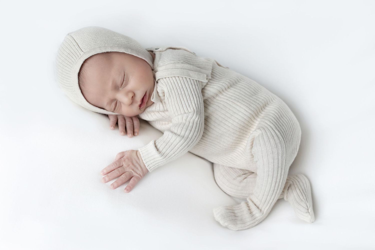 Newborn wearing a knit bonnet sleeping peacefully with his cheek resting on his hand