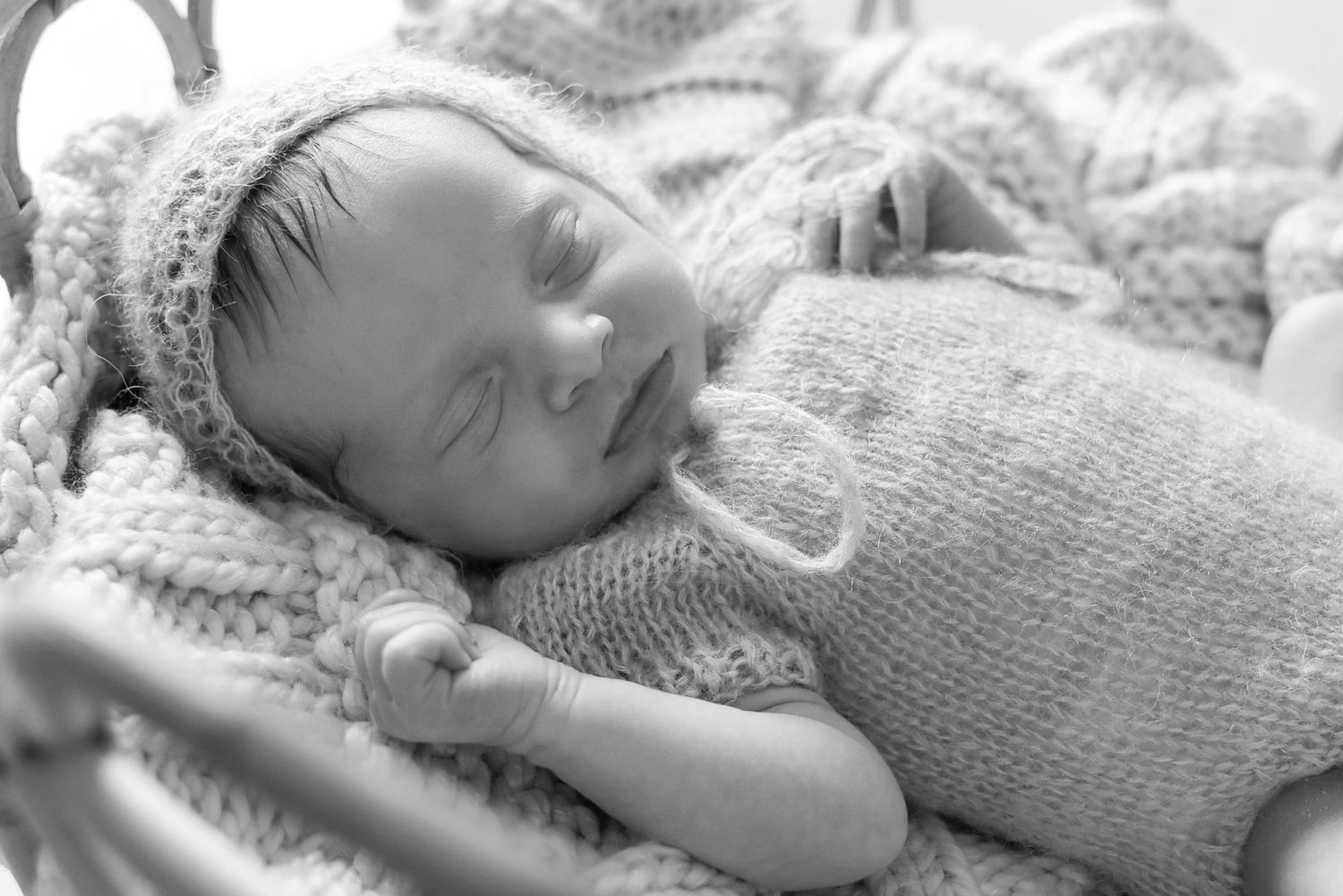 Detailed monochrome shot of a peaceful newborn sleeping on a chunky knit blanket wearing a matching textured outfit