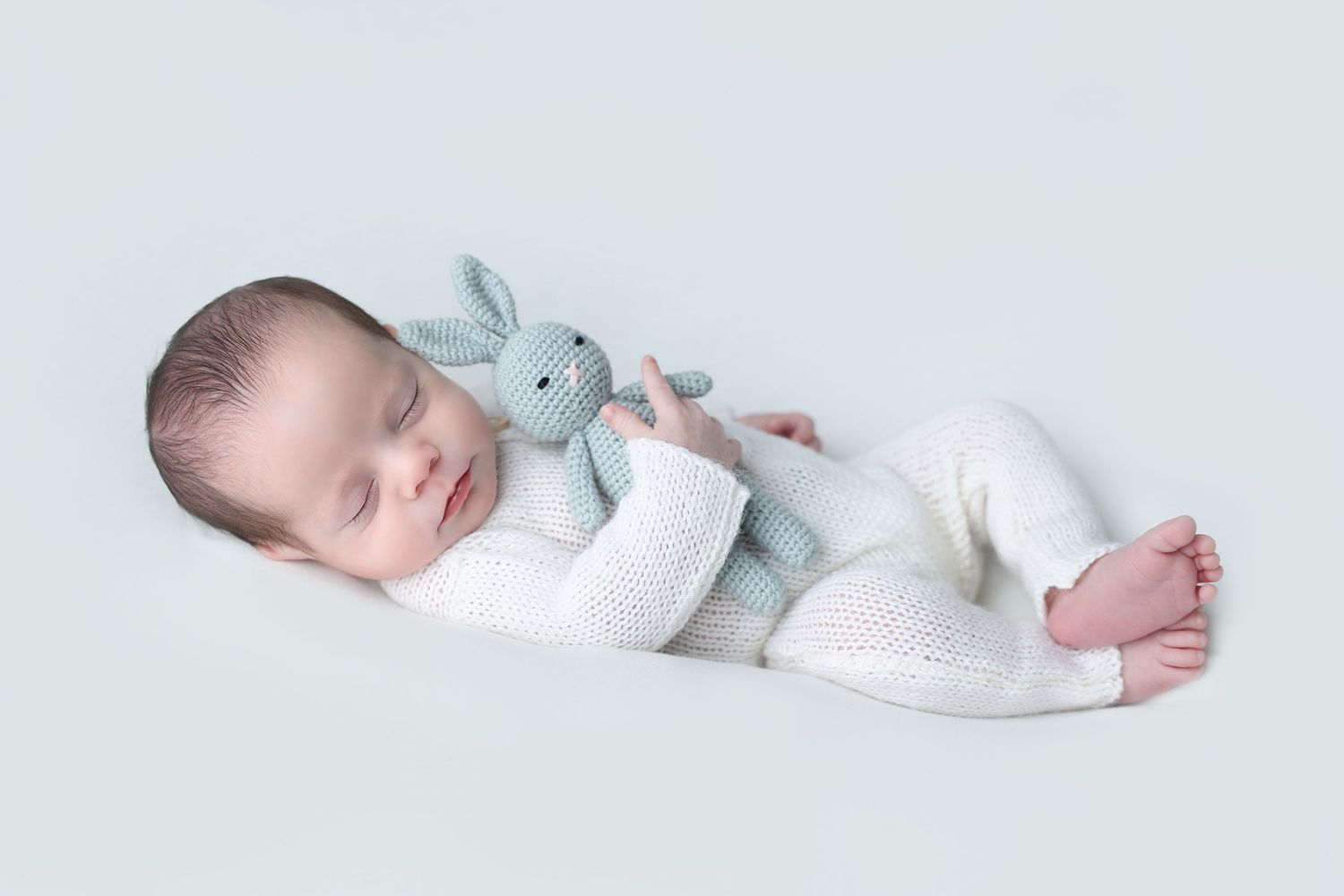 Minimalist newborn photo of a sleeping infant wearing a white knit romper cuddling a handmade bunny lovey