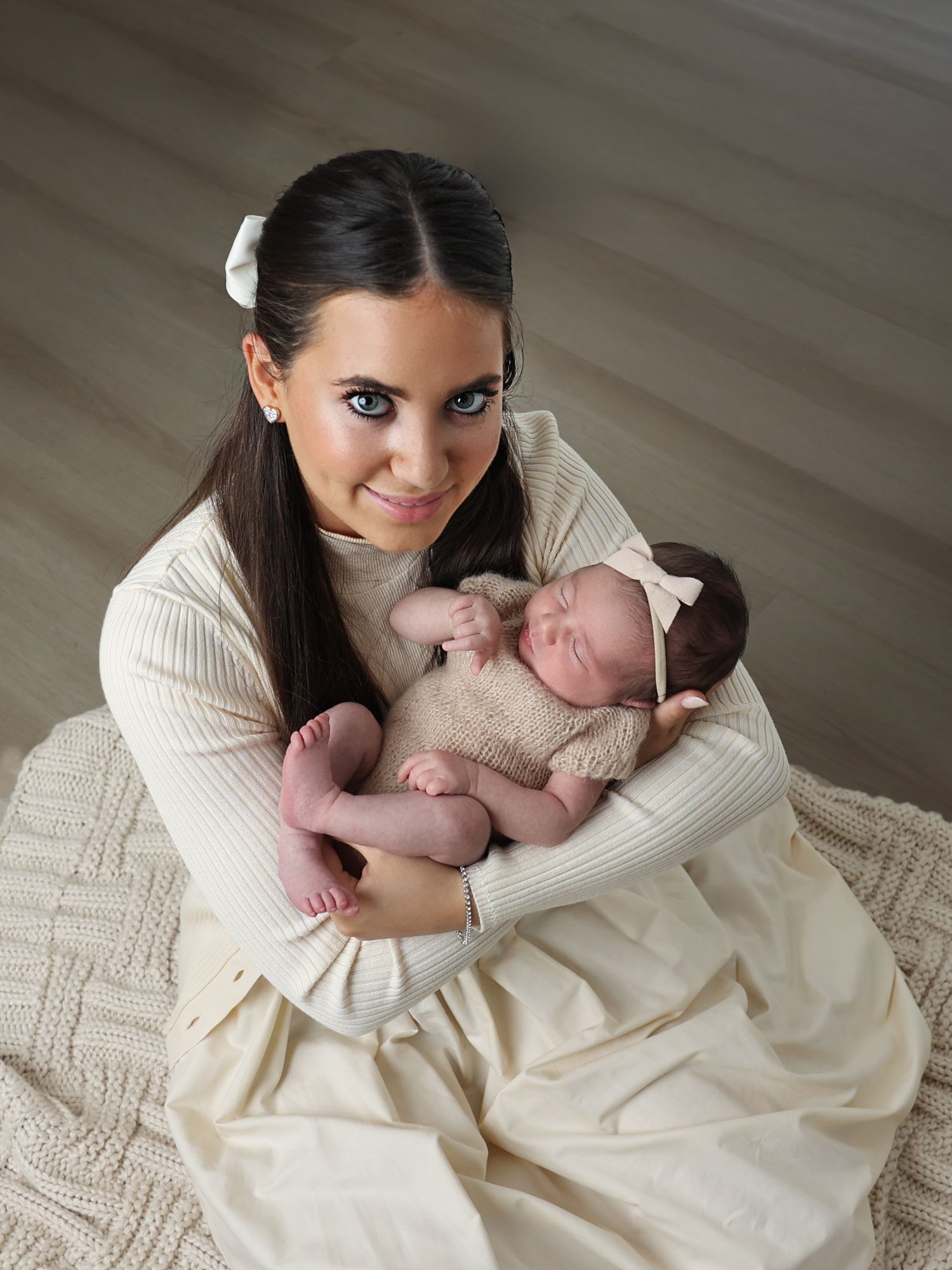 High-angle studio portrait of a proud big sister sitting on the floor cradling her sleeping newborn baby sister